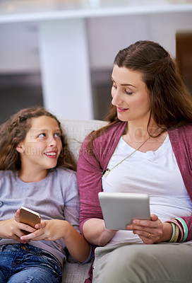 Buy stock photo Cropped shot of a young girll and her mother sitting on the sofa and using their smart devices