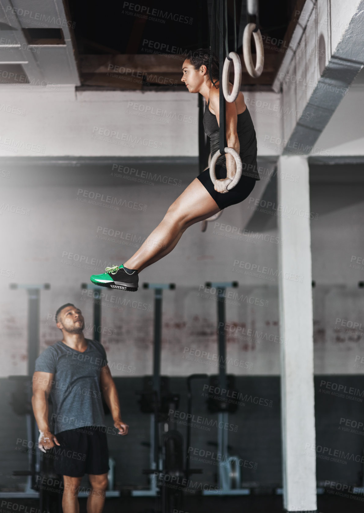 Buy stock photo Full length shot of a young woman working out on the gymnastics rings while her trainer looks on