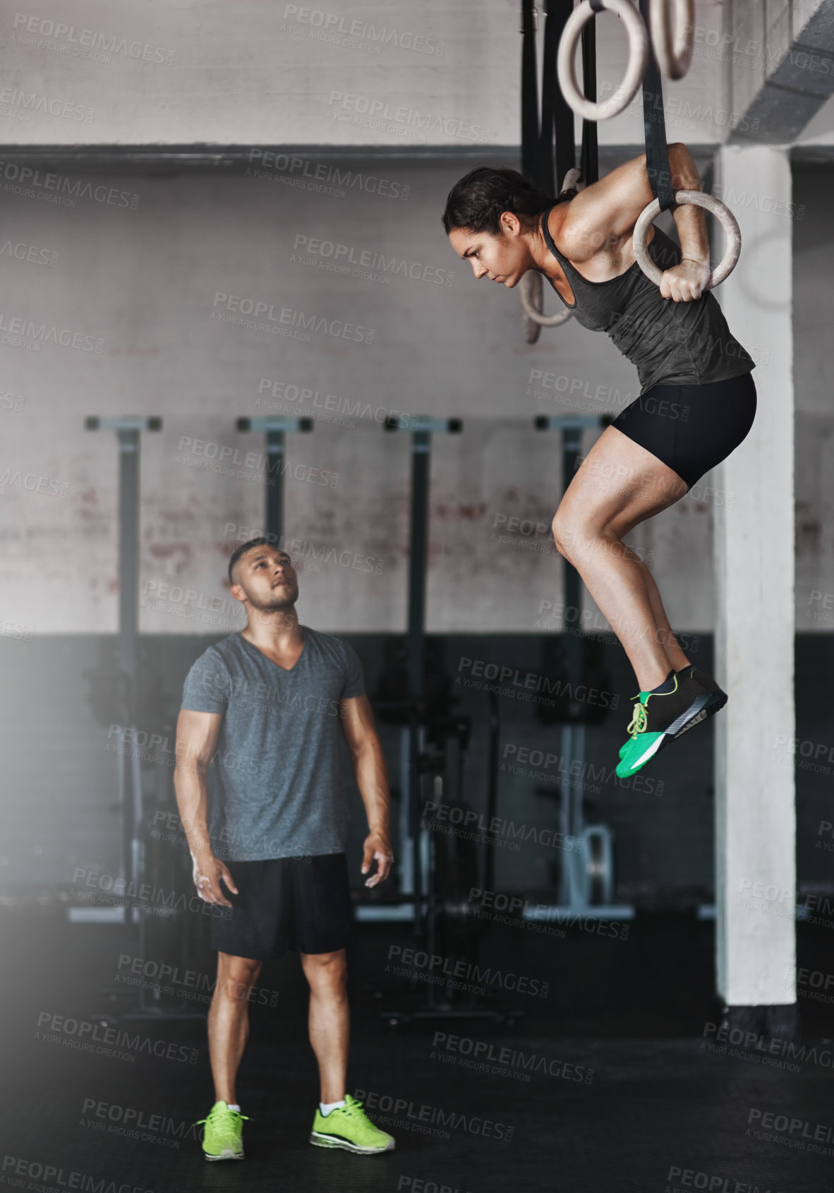 Buy stock photo Full length shot of a young woman working out on the gymnastics rings while her trainer looks on