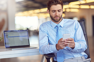 Buy stock photo Shot of a young businessman using his phone in the office