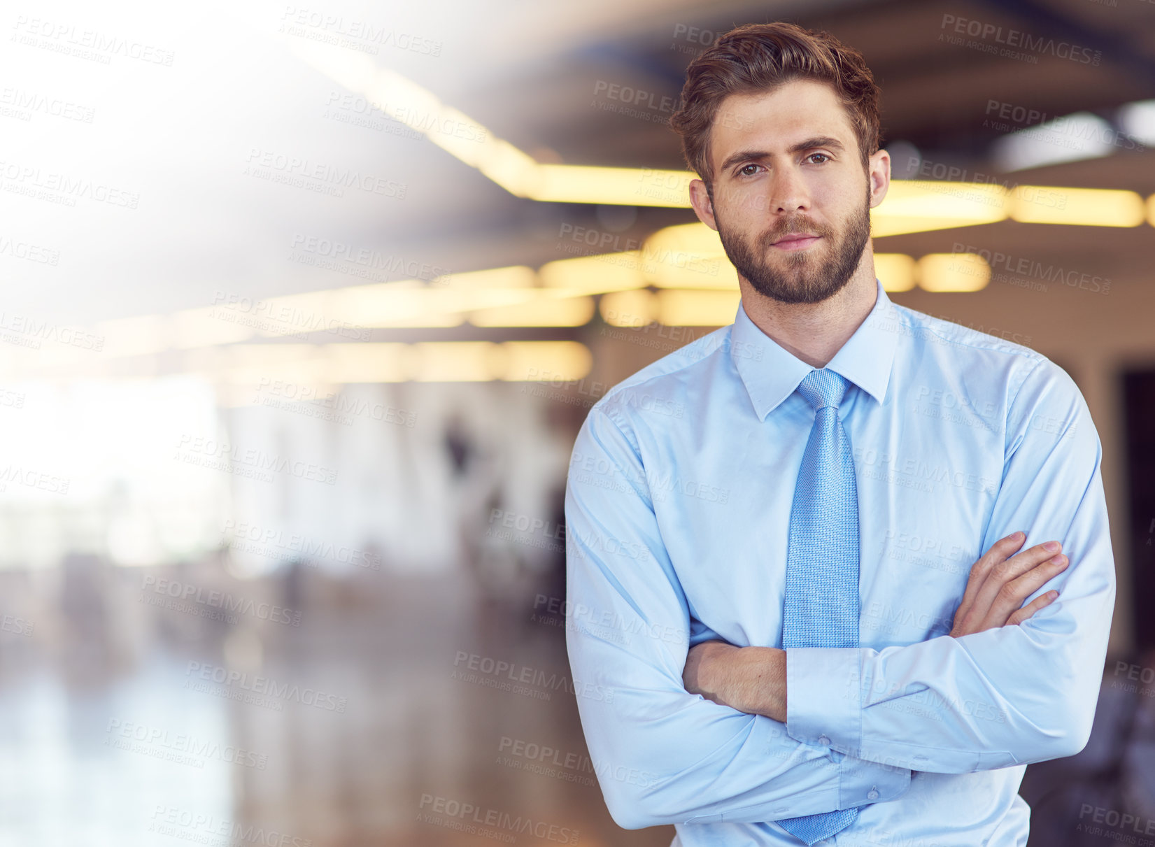 Buy stock photo Portrait of an ambitious young businessman standing with his arms folded in an office