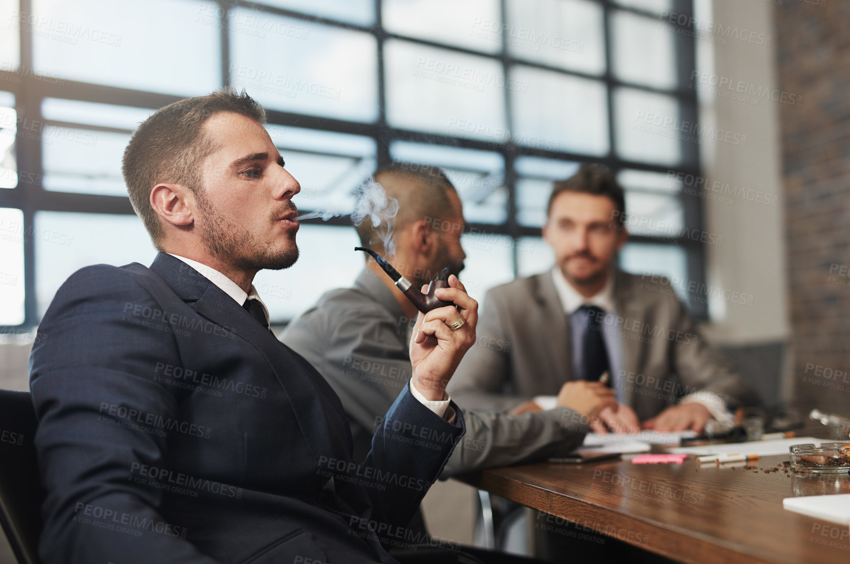 Buy stock photo Shot of a businessman smoking a pipe during a meeting at the office