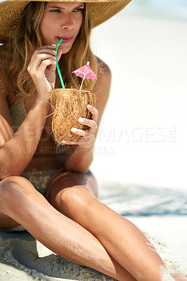 Buy stock photo Cropped shot of a young woman drinking from a coconut while relaxing at the beach