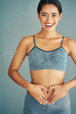 Buy stock photo Woman, stomach and heart in studio portrait, gut health and symbol for colon wellness on blue background. Female person, hands and abdomen for digestion, love emoji and detox for progress in fitness