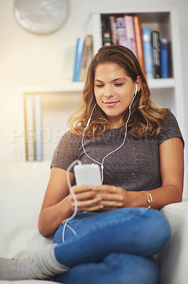 Buy stock photo Shot of a young woman listening to music on her phone at home