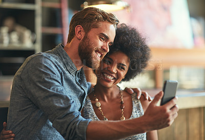 Buy stock photo Shot of a young couple taking a selfie on a mobile phone at a cafe