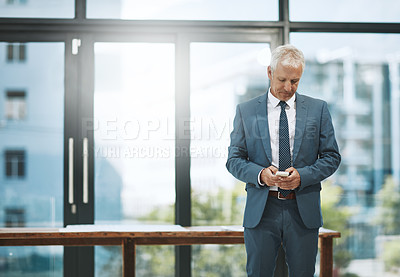 Buy stock photo Cropped shot of a mature businessmen sending a text while standing in his office