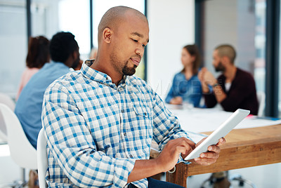 Buy stock photo Shot of a young man using his  tablet with his colleagues sitting in the background