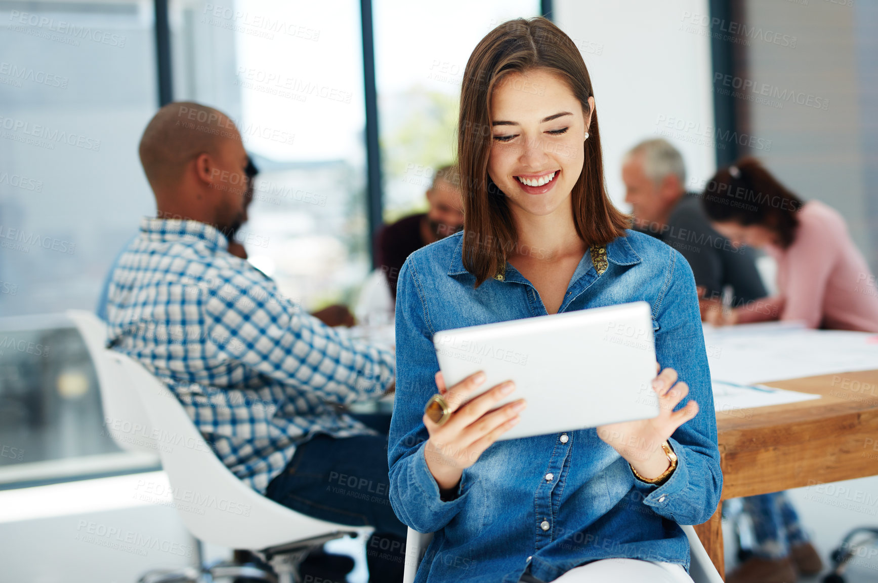 Buy stock photo Shot of a young woman using her tablet with her colleagues sitting in the background