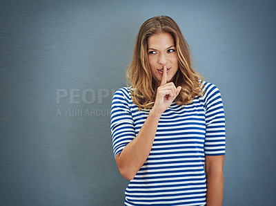 Buy stock photo Studio shot of a young woman covering her lips with her finger against a gray background