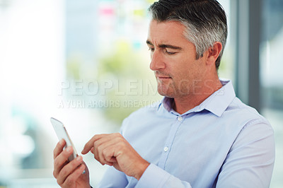 Buy stock photo Cropped shot of a mature businessman using his cellphone while sitting in the office