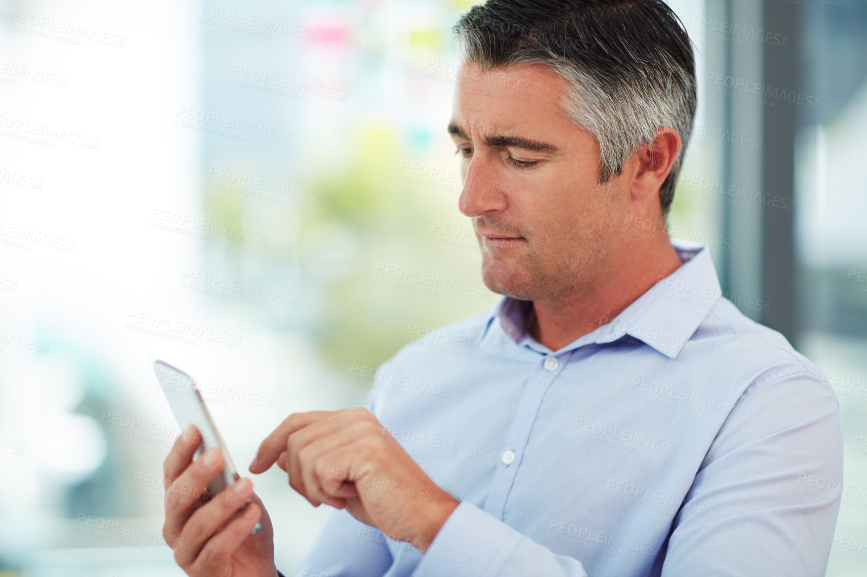 Buy stock photo Cropped shot of a mature businessman using his cellphone while sitting in the office