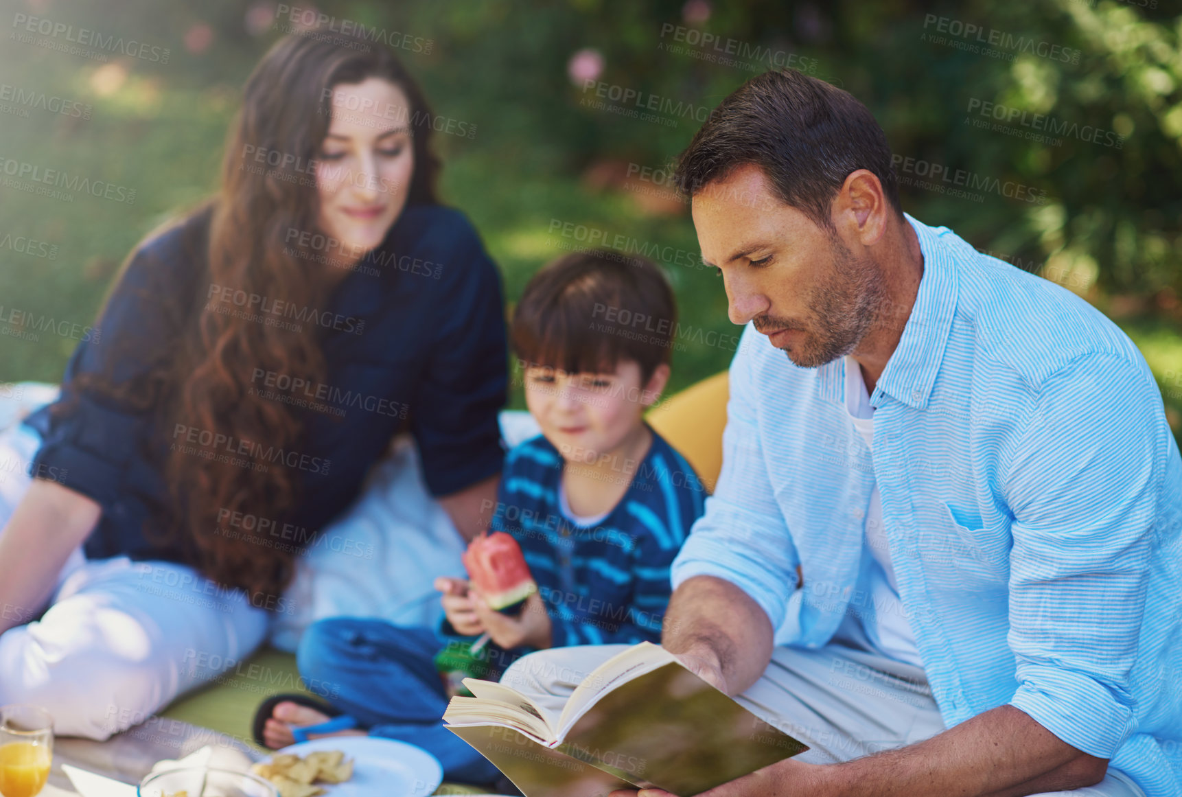 Buy stock photo Shot of a parents reading a book to their son during a picnic in the park