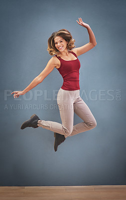 Buy stock photo Shot of a happy young woman jumping in the air against a gray background