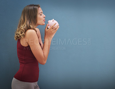 Buy stock photo Shot of a young woman kissing a piggybank against a gray background