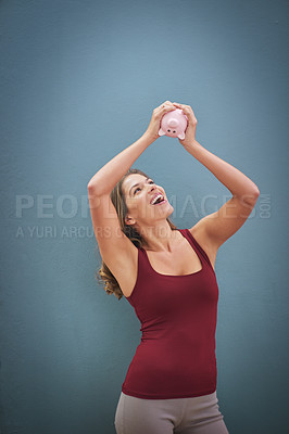 Buy stock photo Shot of a smiling young woman holding a piggybank in the air against a gray background