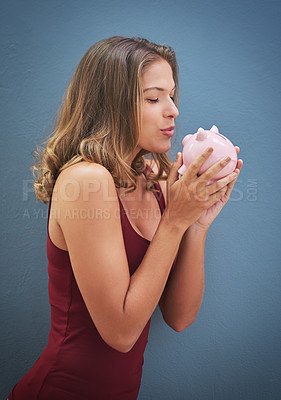 Buy stock photo Shot of a young woman kissing a piggybank against a gray background