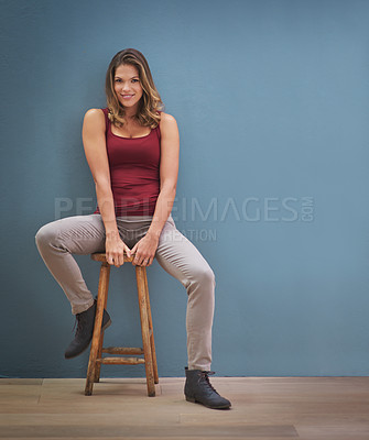 Buy stock photo Portrait of a young woman sitting in a chair in front of a gray background