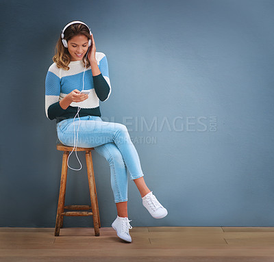 Buy stock photo Shot of a young woman sitting on a stool and listening to music