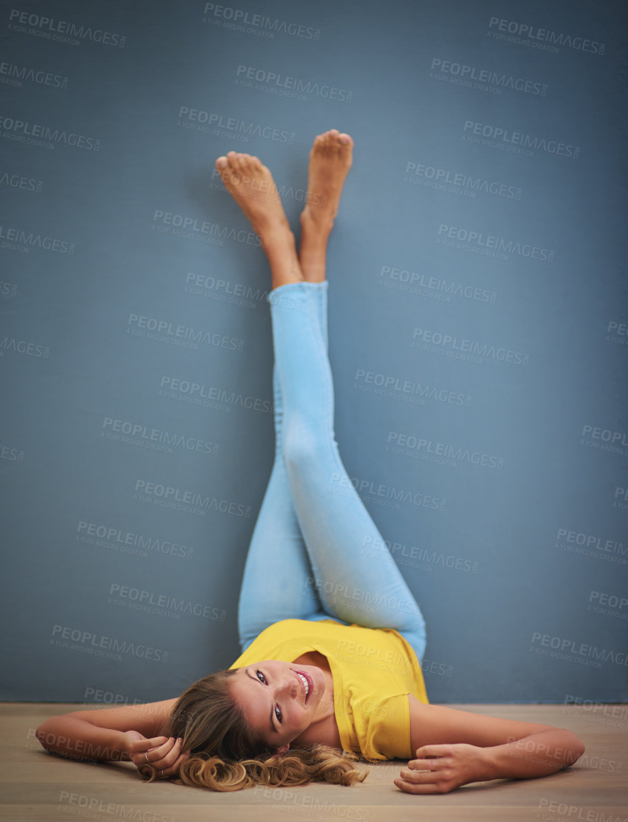 Buy stock photo Relax, portrait and woman with legs on wall for calm, peace and harmony on weekend morning. Mockup space, smile and happy female person resting and laying on floor in apartment by blue background.