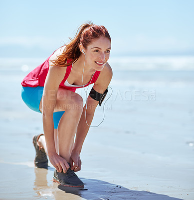 Buy stock photo Full length shot of a young woman tying her laces while running on the beach