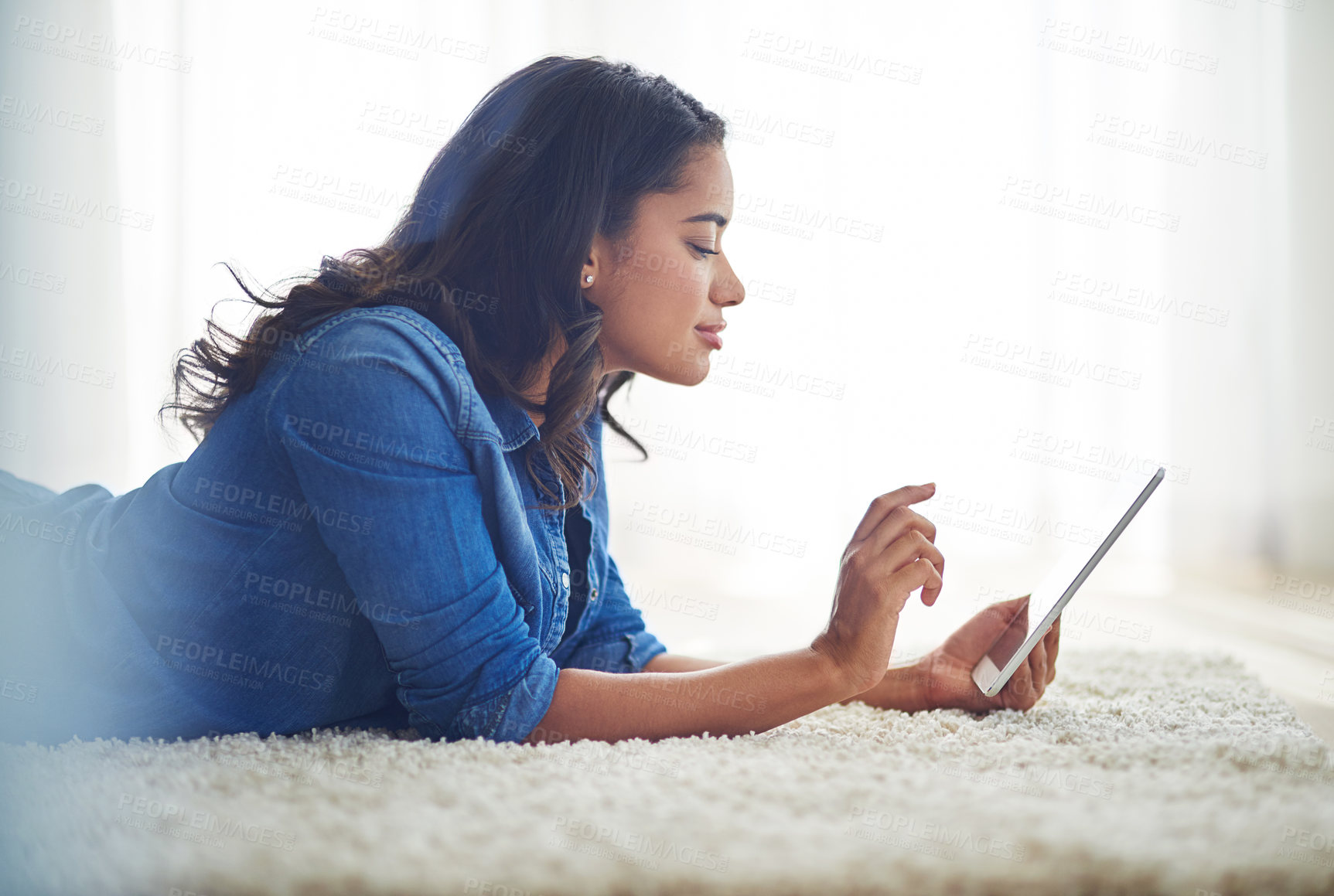 Buy stock photo Shot of a young woman browsing the web on her tablet at home