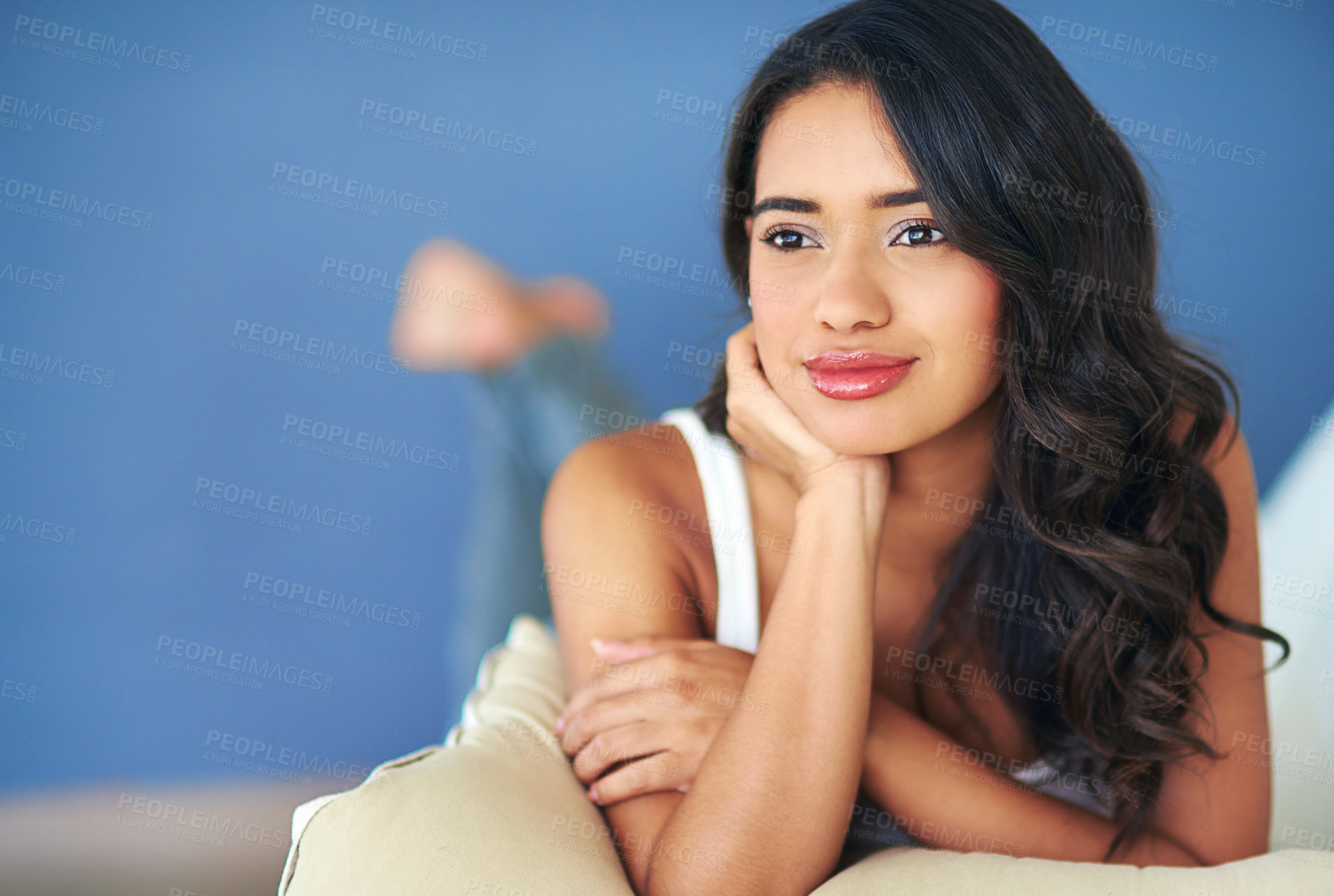 Buy stock photo Shot of a young woman looking thoughtful while lying on her living room sofa