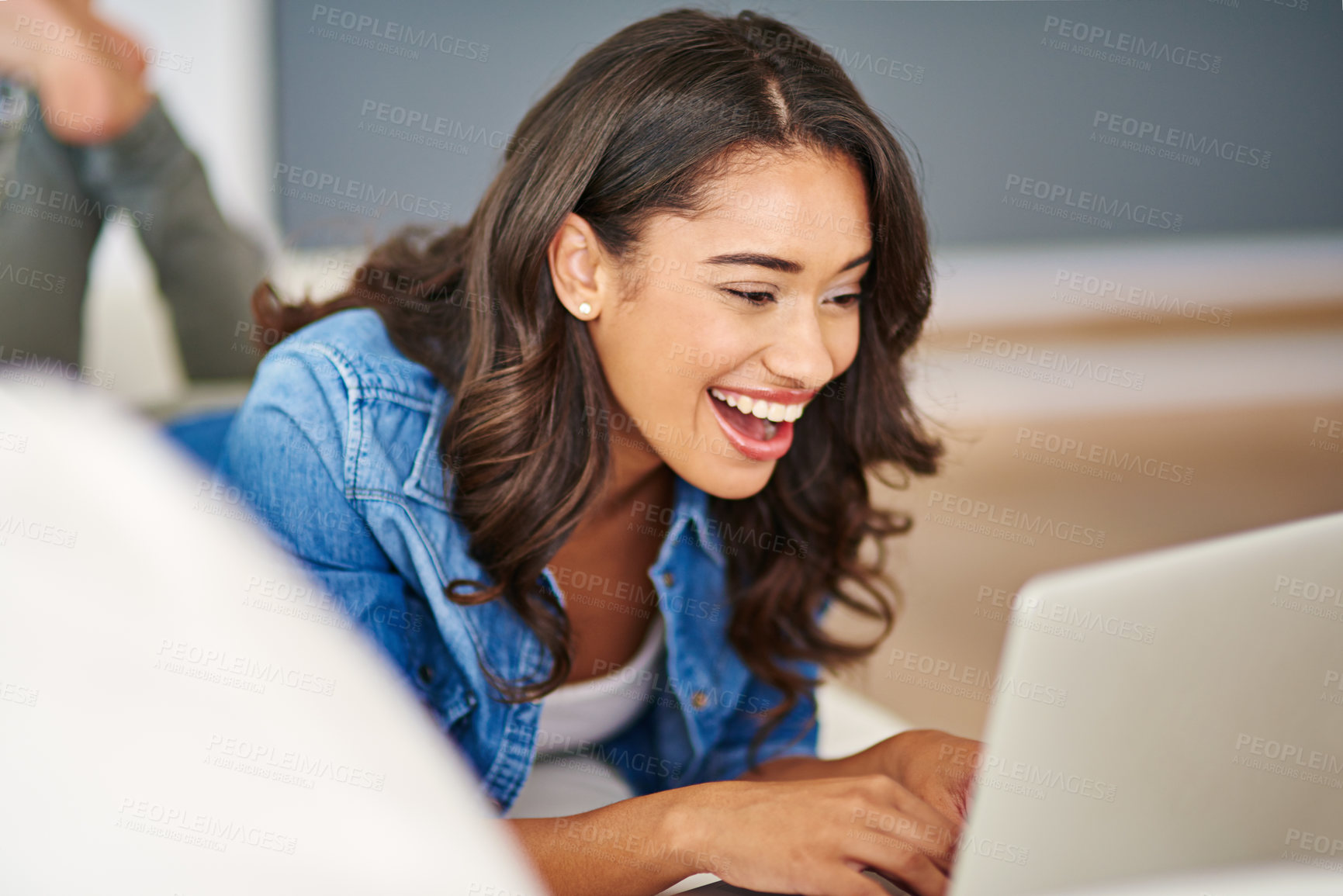 Buy stock photo Cropped shot of an attractive young woman using her laptop while lying on the sofa