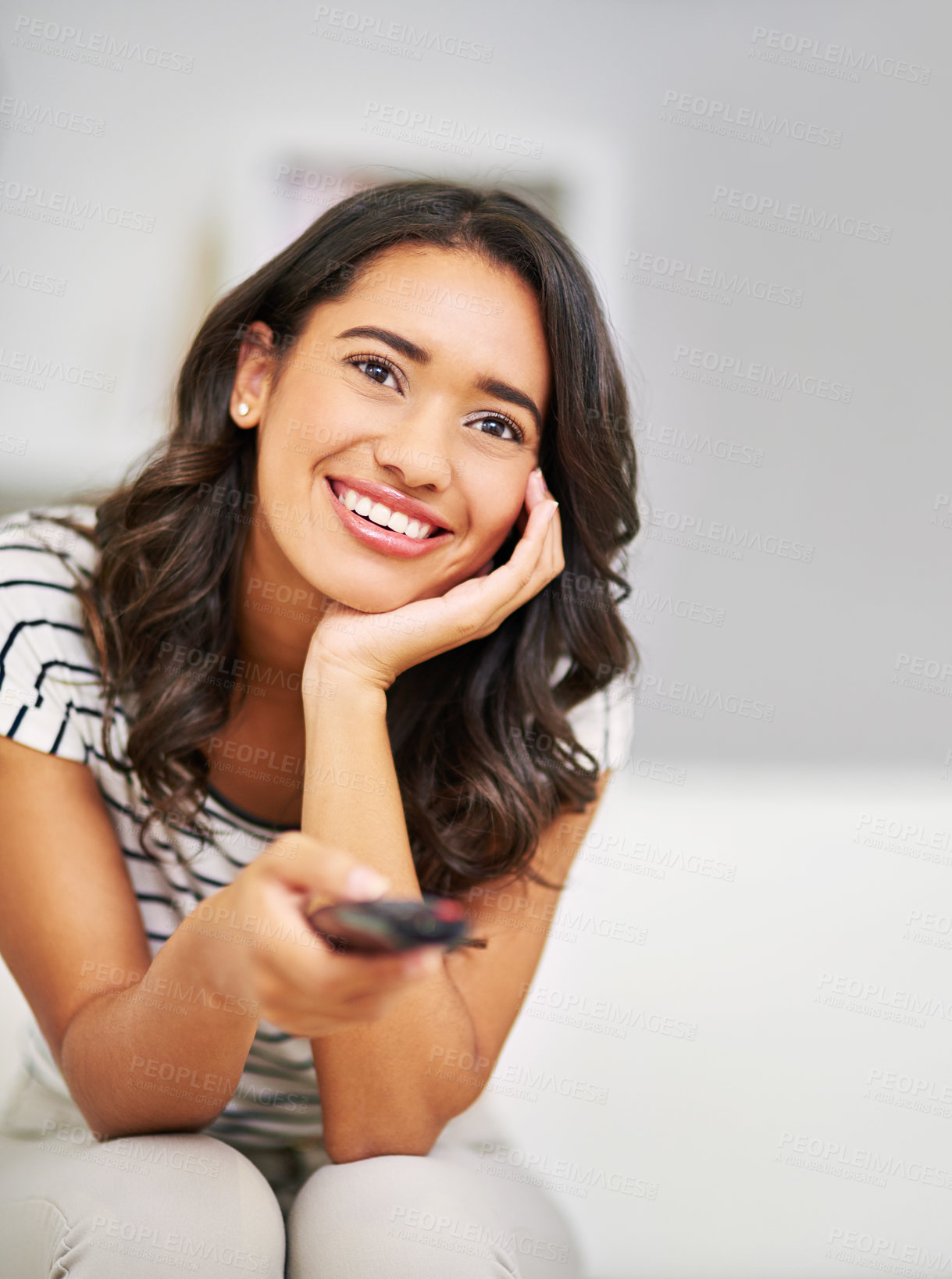Buy stock photo Cropped shot of a young woman watching TV while relaxing on her sofa at home
