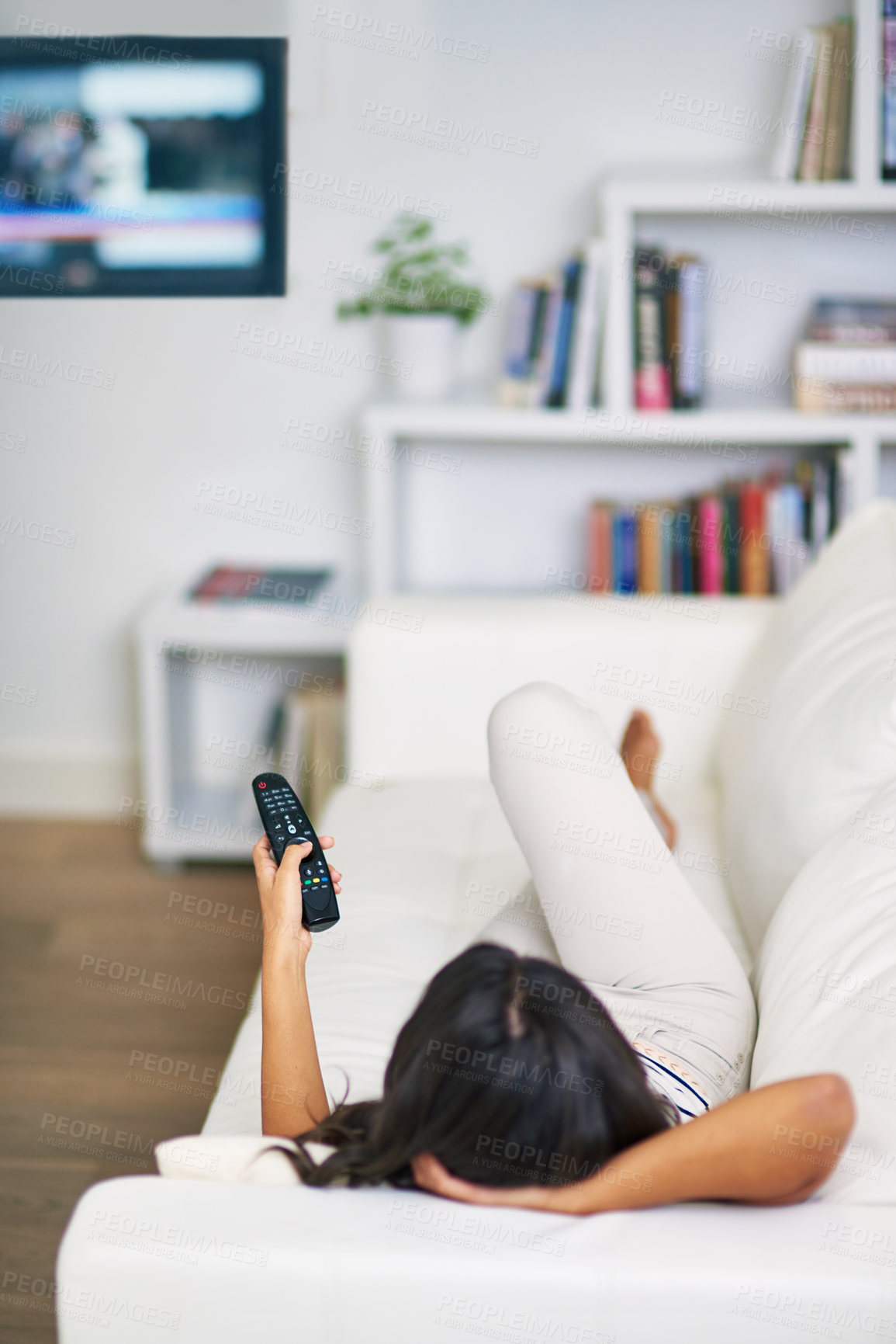 Buy stock photo Shot of a young woman watching TV while relaxing on her sofa at home