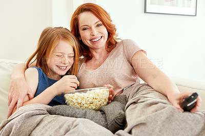 Buy stock photo Shot of a mature woman and her young daughter watching a movie and eating popcorn on the sofa