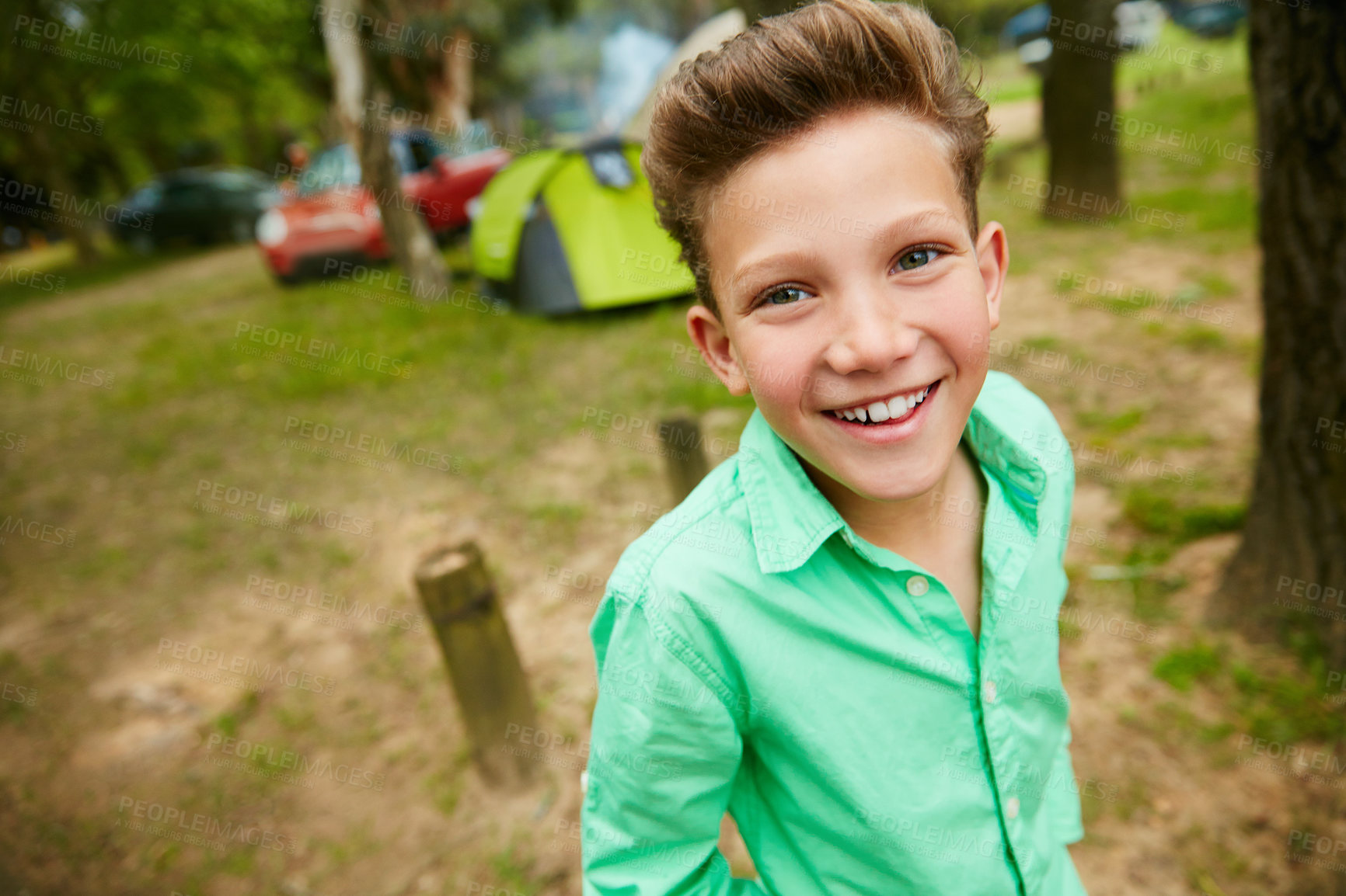 Buy stock photo Portrait of a cute boy child on a camping trip. Closeup of smiling kid having fun while in a forest with tents in the background. Cheerful kid excited about spending time in nature