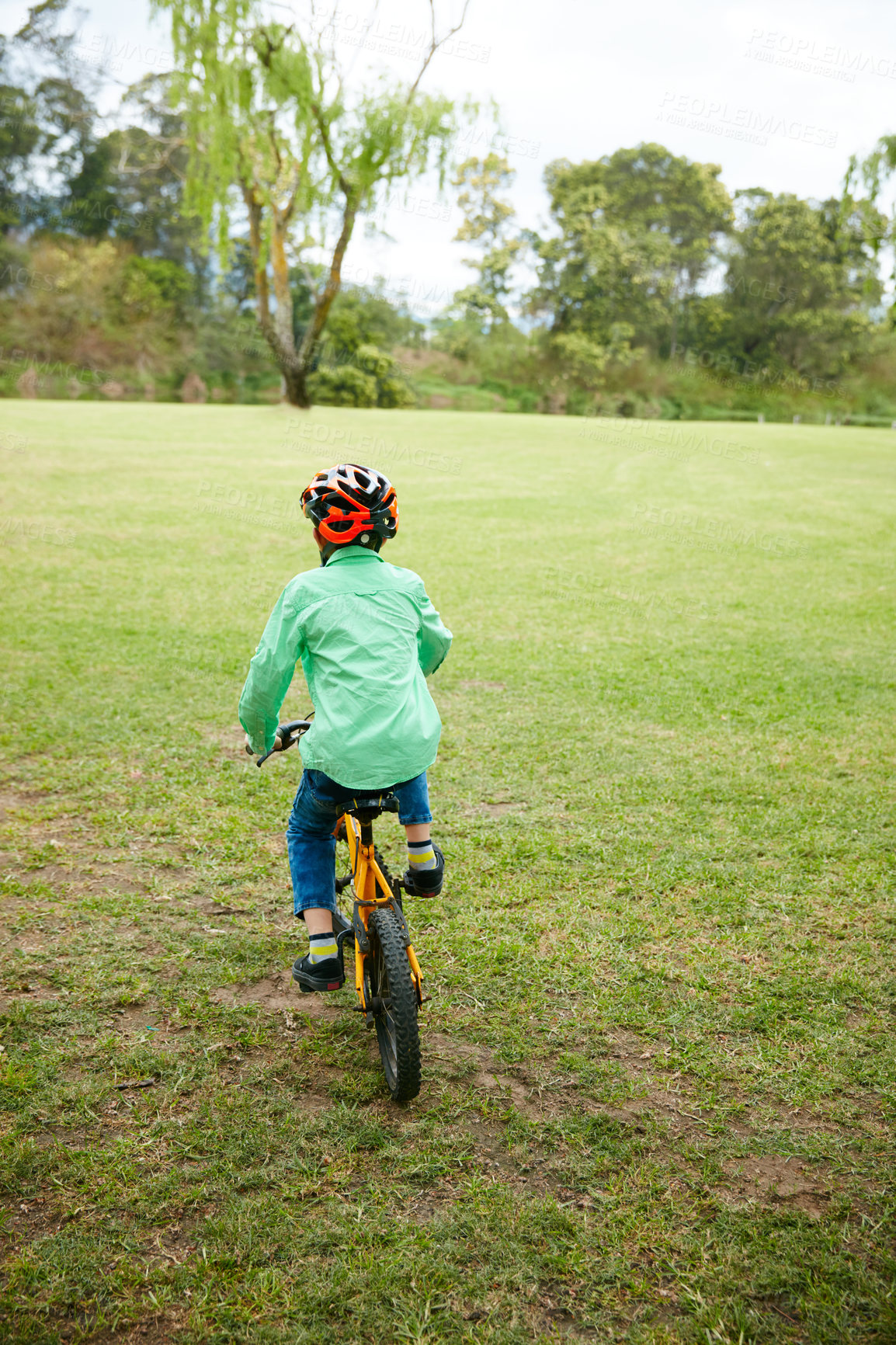 Buy stock photo Rearveiw shot of a young boy riding his bike in a park