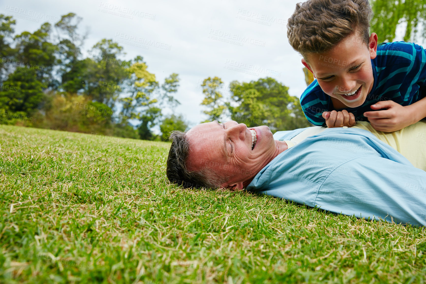 Buy stock photo Shot of a laughing father and son lying on grass