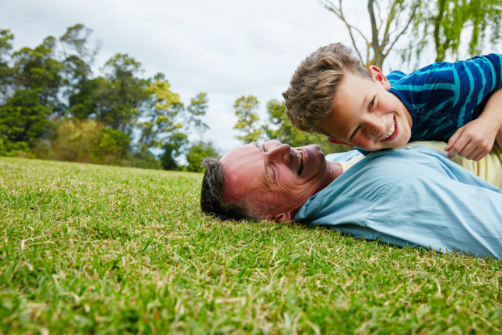 Buy stock photo Shot of a laughing father and son lying on grass