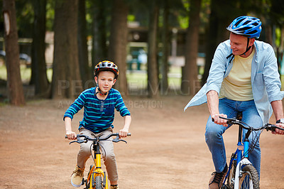 Buy stock photo Shot of a father and his young son riding bicycles through a park