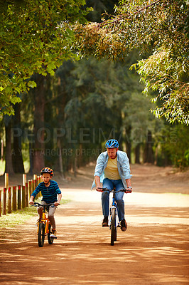 Buy stock photo Shot of a father and his young son riding bicycles through a park