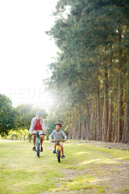 Buy stock photo Shot of a father and son riding bicycles in a park