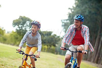 Buy stock photo Shot of a father and son riding bicycles in a park