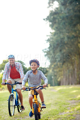 Buy stock photo Shot of a father and son riding bicycles in a park