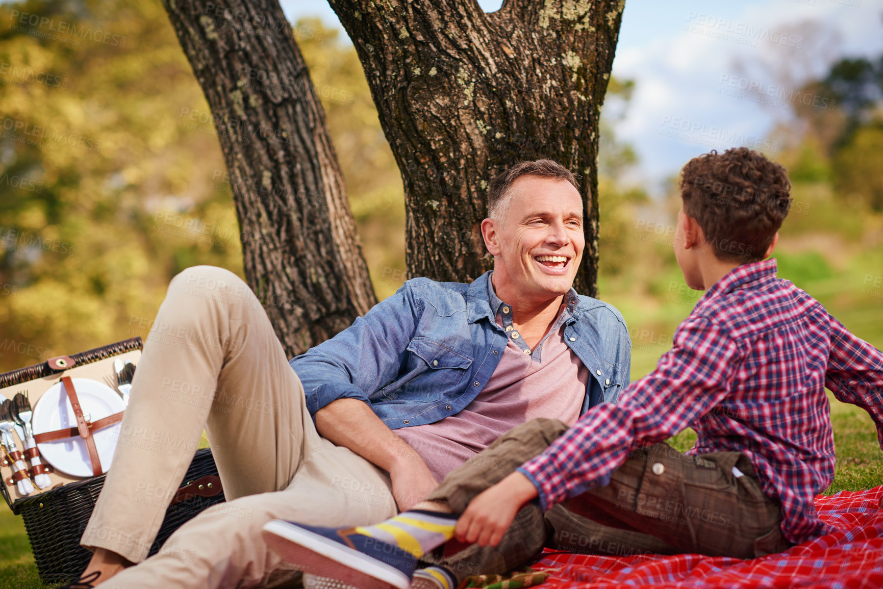 Buy stock photo Shot of a father and son talking together while lying in a park