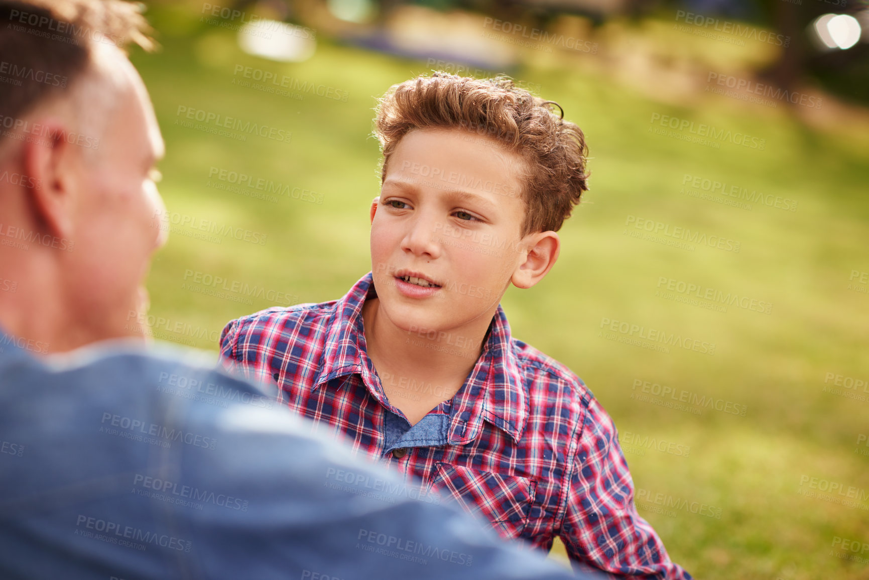 Buy stock photo Shot of a father and son talking together while lying in a park