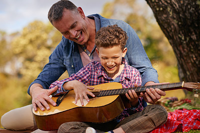 Buy stock photo Shot of a father teaching his son how to play guitar while sitting outside
