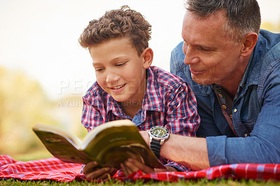 Buy stock photo Shot of a father and son reading a book together in a park