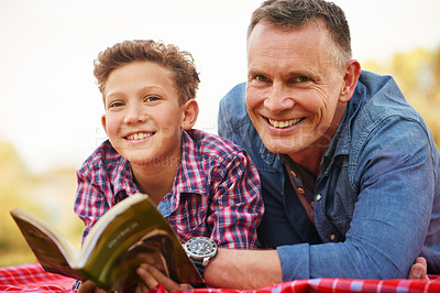 Buy stock photo Portrait of a father and son reading a book together in a park