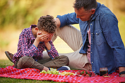 Buy stock photo Shot of a father comforting his young son while sitting in a park