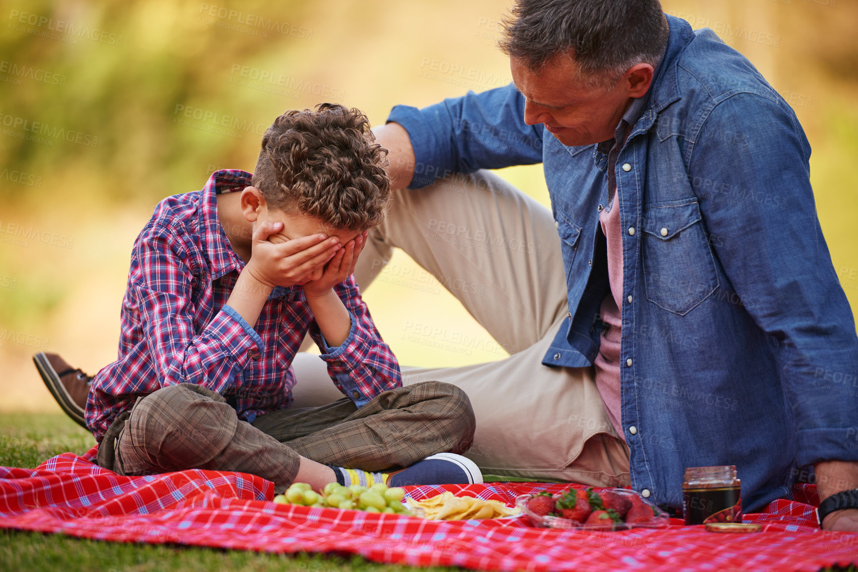 Buy stock photo Shot of a father comforting his young son while sitting in a park