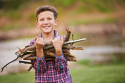 Buy stock photo Portrait of young boy carrying a bundle of sticks for a fire while camping. Happy child collecting firewood in the forest for a campfire. Boy looking for old tree branches while camping in nature 