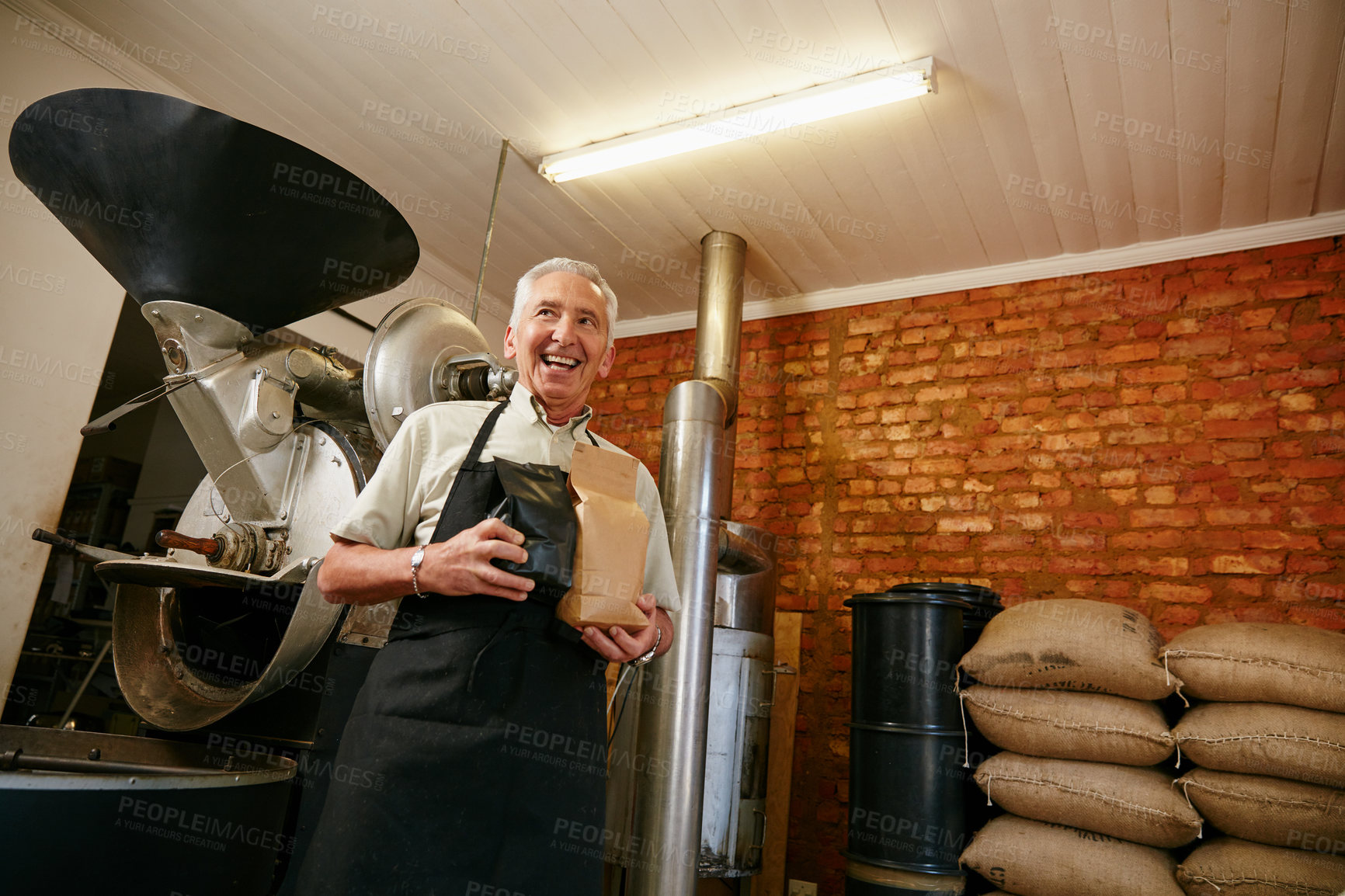 Buy stock photo Low angle portrait of a senior man holding bags of coffee beans while working in a roastery