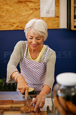 Buy stock photo Shot of a senior woman cutting a slice of cake in a bakery